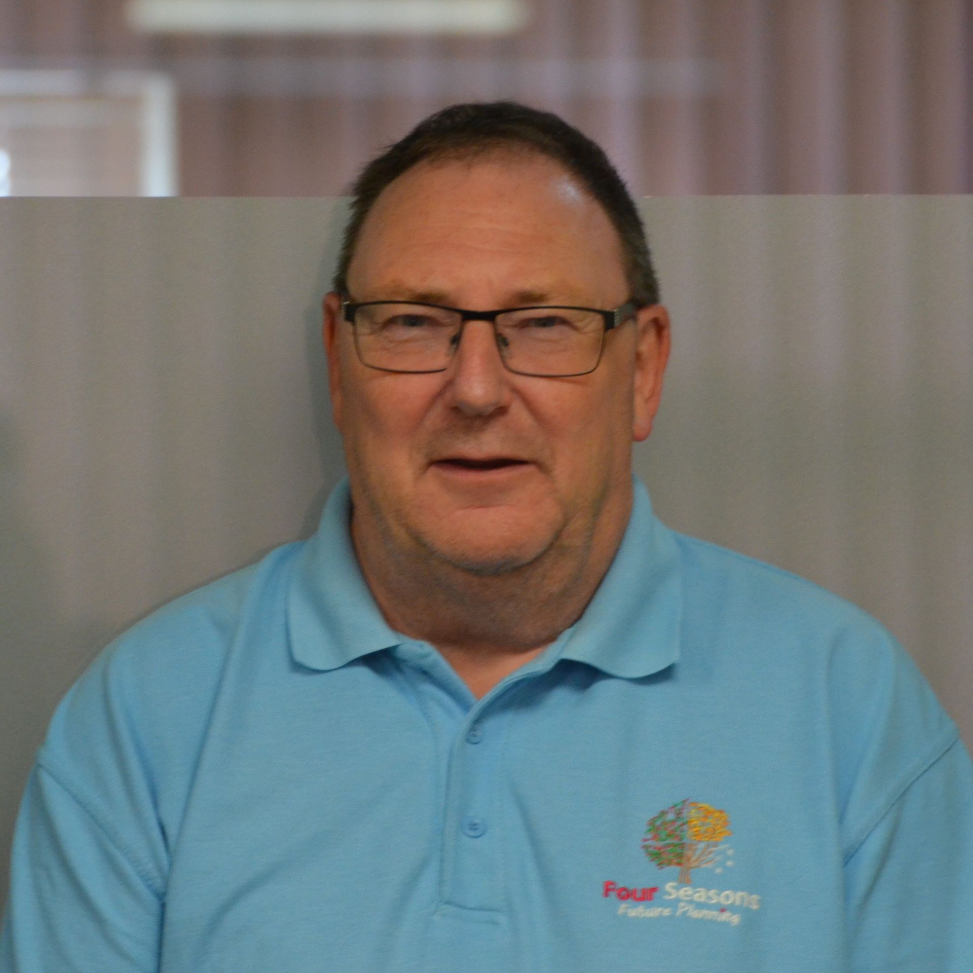 A man wearing glasses and a blue shirt that says ' four seasons ' on it