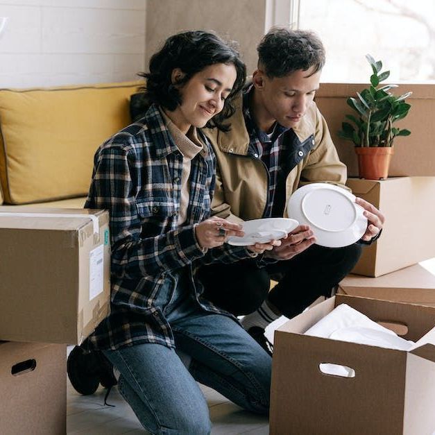 A man and a woman are sitting on the floor looking at plates.