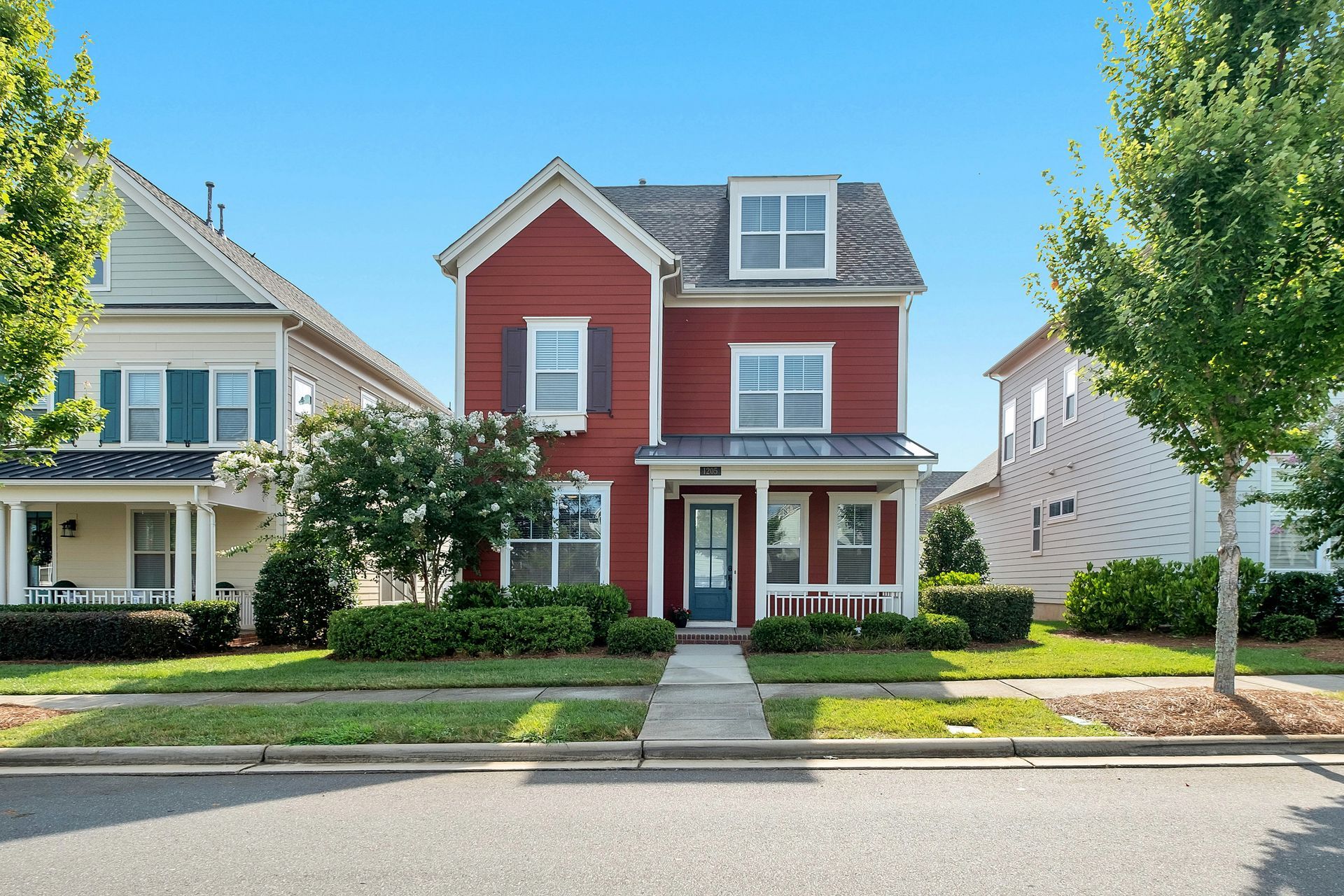A red house with white shutters and a blue door is in a residential neighborhood.