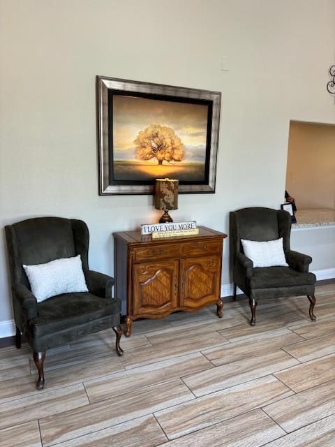Two green armchairs flanking a wooden cabinet with a painting of a tree above it.