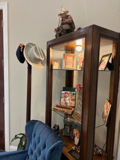 Wooden display cabinet with photos and figurines, next to a hat stand with two hats.