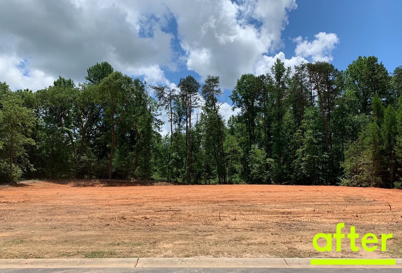 Cleared red dirt lot in front of a treeline, under a cloudy blue sky. 