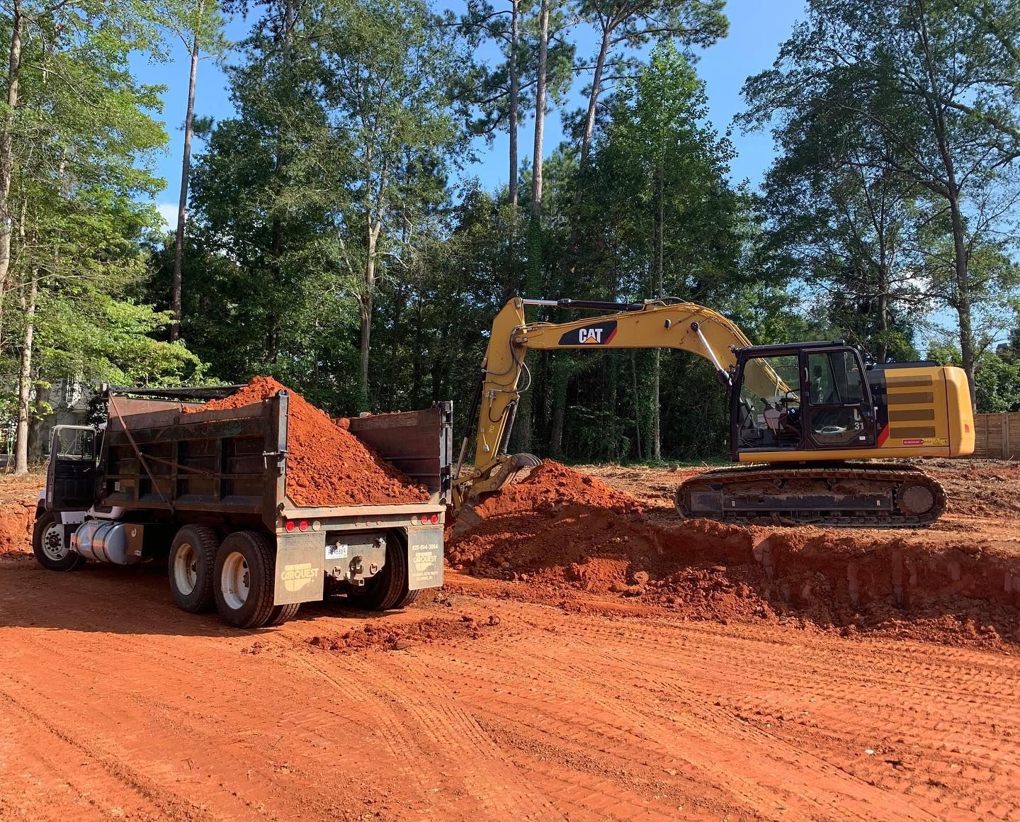 Yellow excavator loading red soil into a dump truck at a construction site.