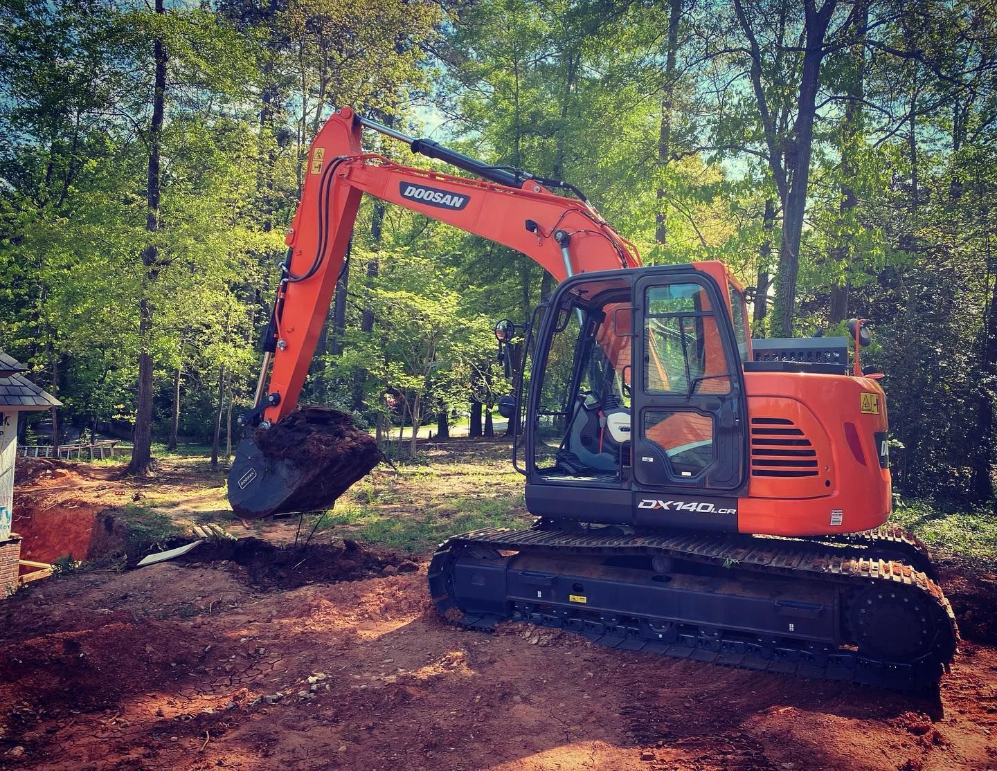 Orange excavator digging in a dirt area, trees in the background.