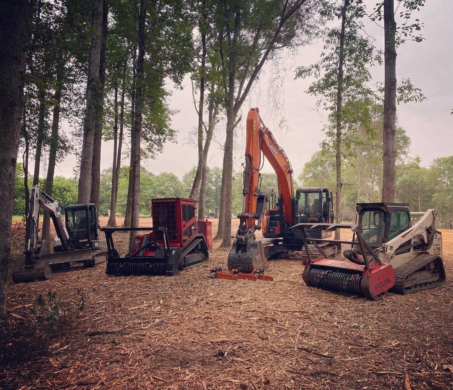 Five pieces of heavy machinery in a wooded area, likely for land clearing or forestry work.