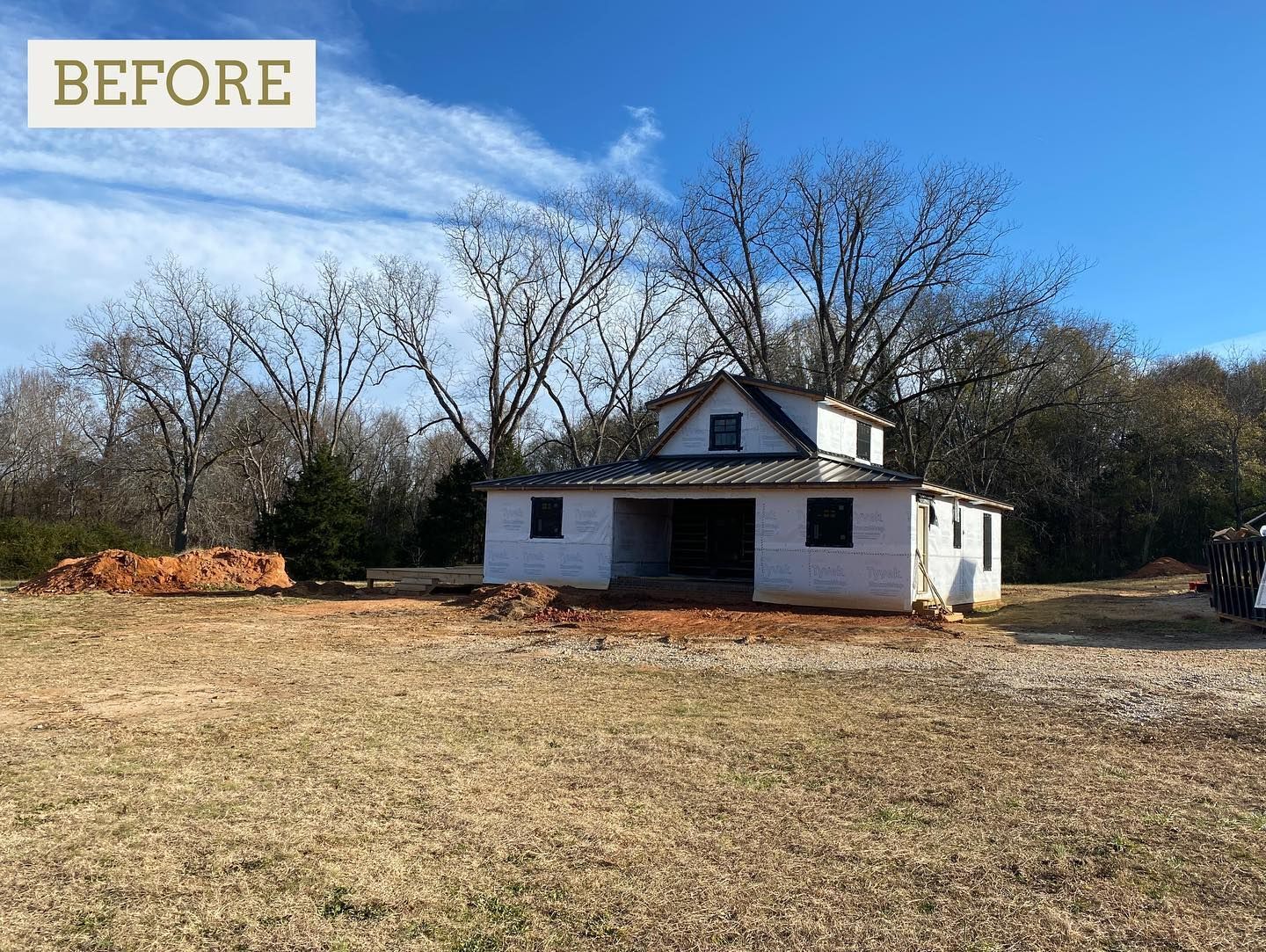 A white, two-story building in a field with bare trees and a blue sky; 