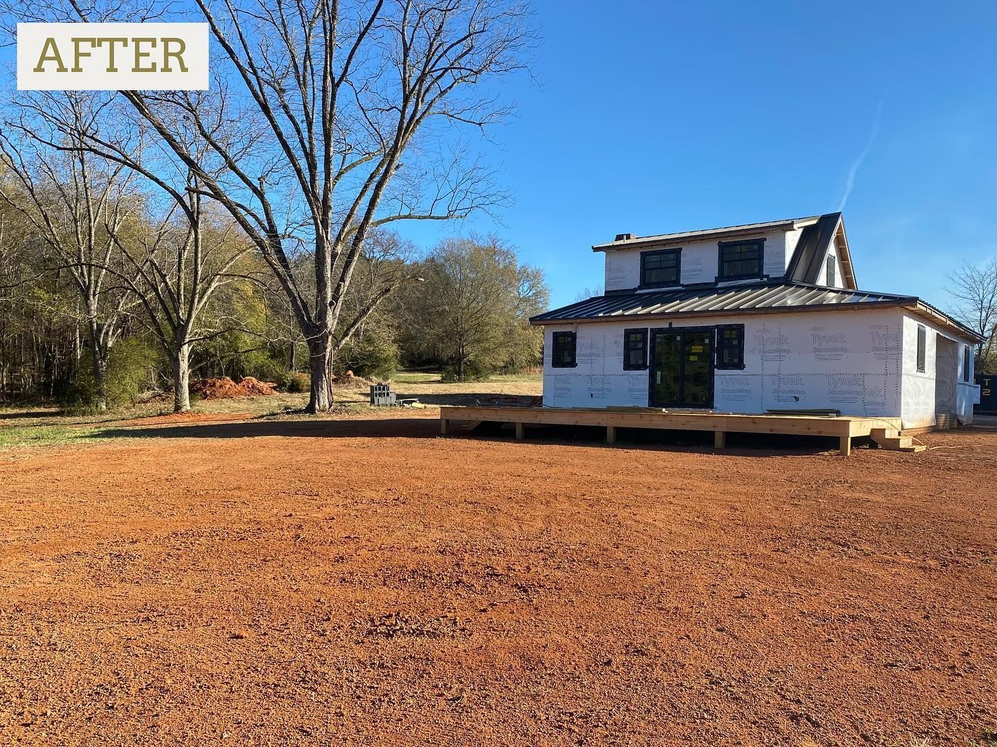 Newly constructed house with a deck in a yard with red gravel; clear sky.