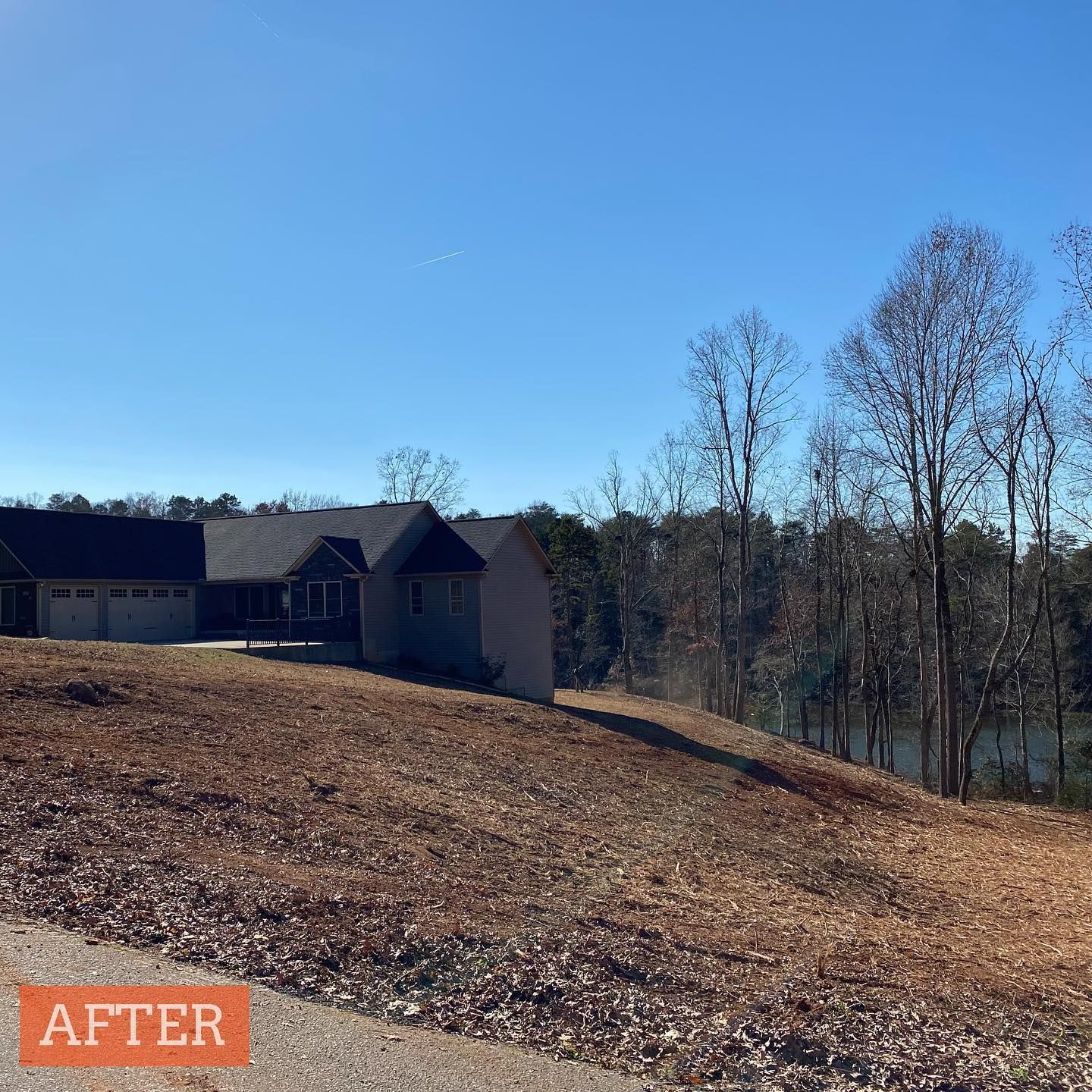 Newly constructed house on a hill with bare trees, dry leaves, and a blue sky.