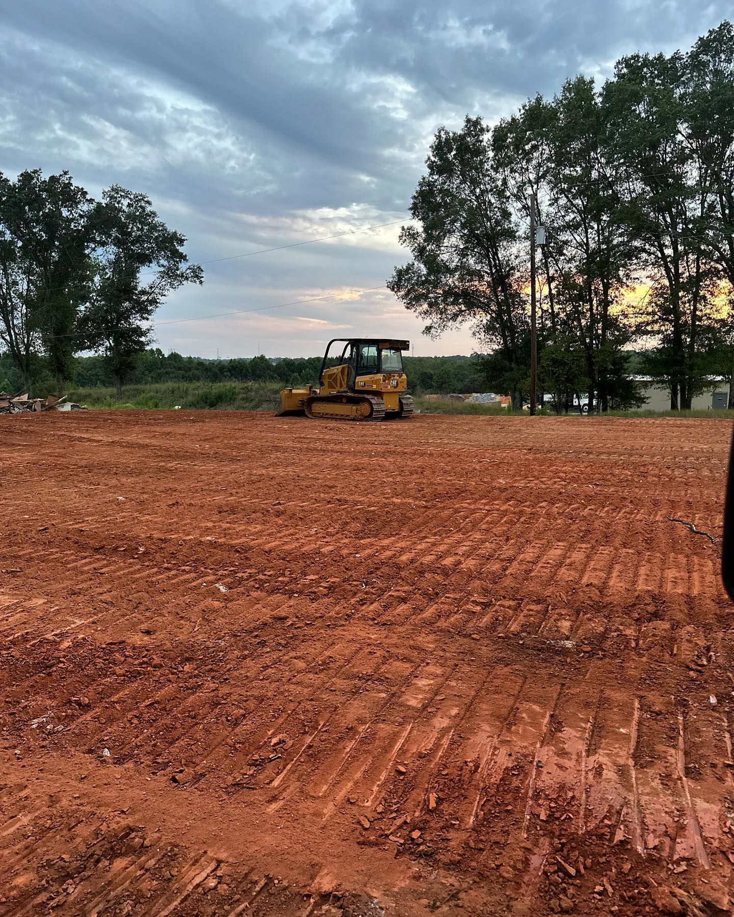 Yellow bulldozer on a freshly cleared red dirt field under a cloudy sky.
