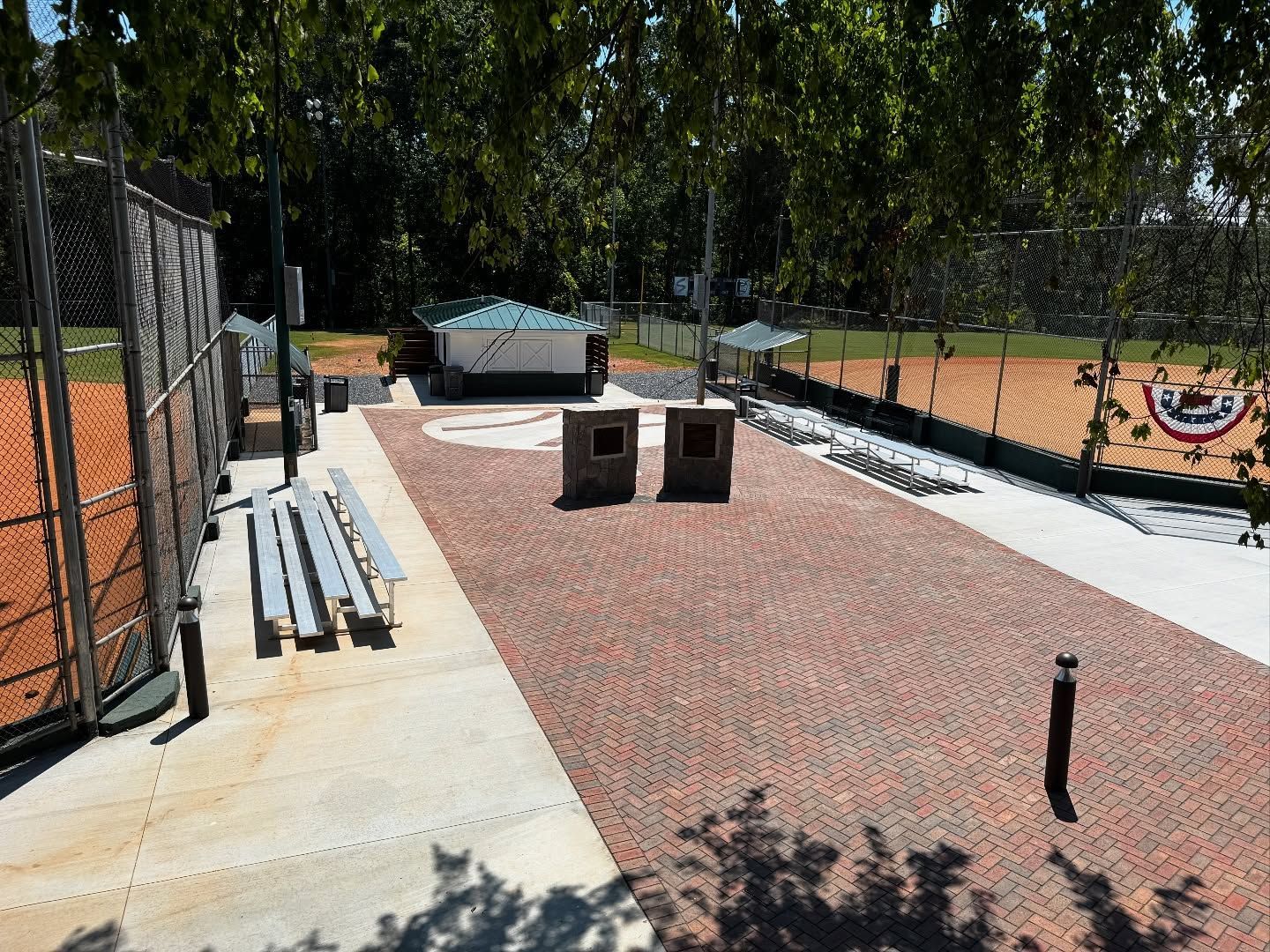 Baseball field with brick path, benches, trash cans, and dugout under a bright sky.