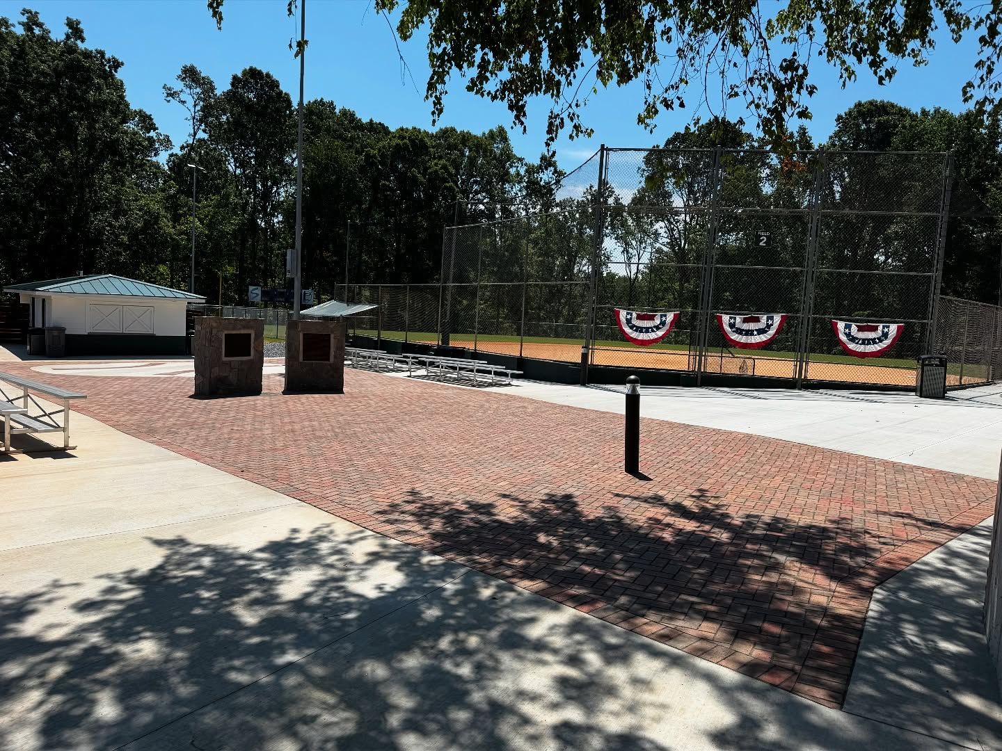 Baseball field with red brick ground, stands, and netting.