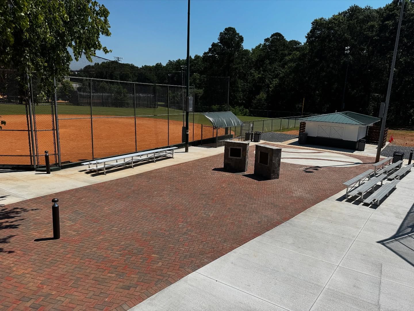 Softball field with brick patio, bleachers, and dugout, under a clear sky.