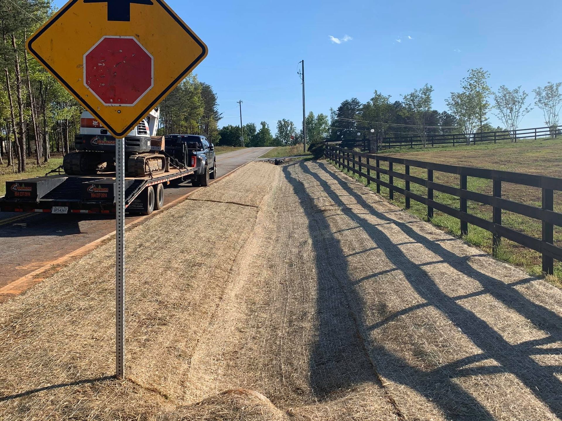 Gravel road being constructed. A trailer with tires parked nearby, and a stop sign on a post in the foreground.