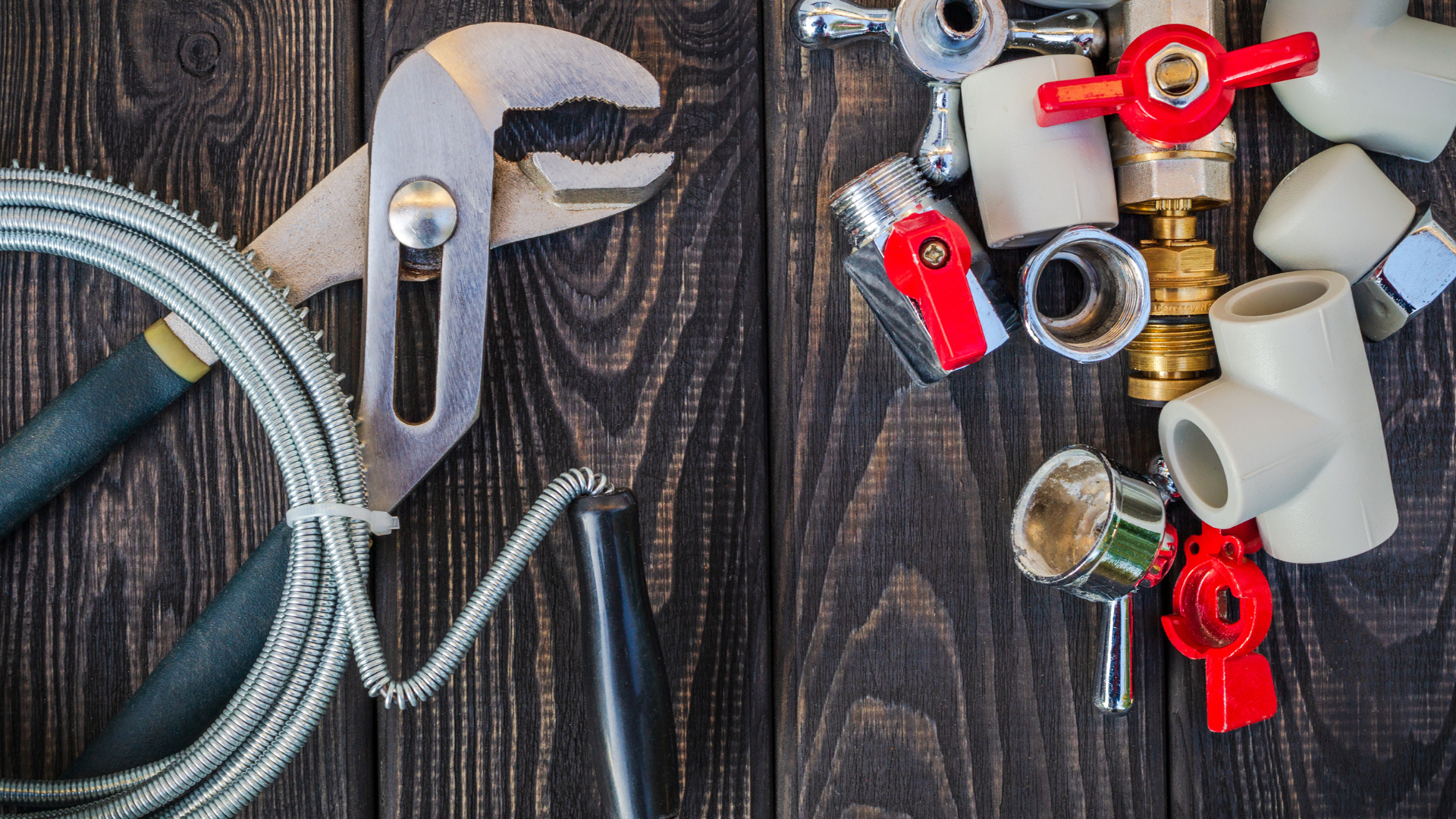 Plumbing tools and parts: pliers, tubing, valves, and fittings arranged on a dark wood surface.