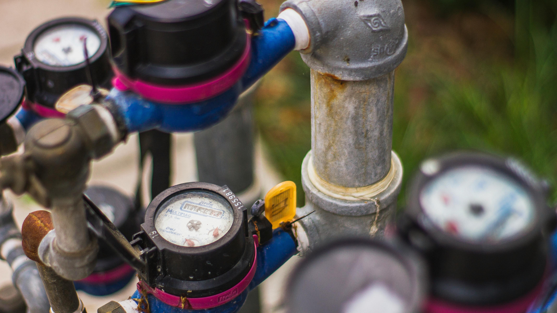 Close-up of water meters and pipes with black and blue connections, set outdoors.