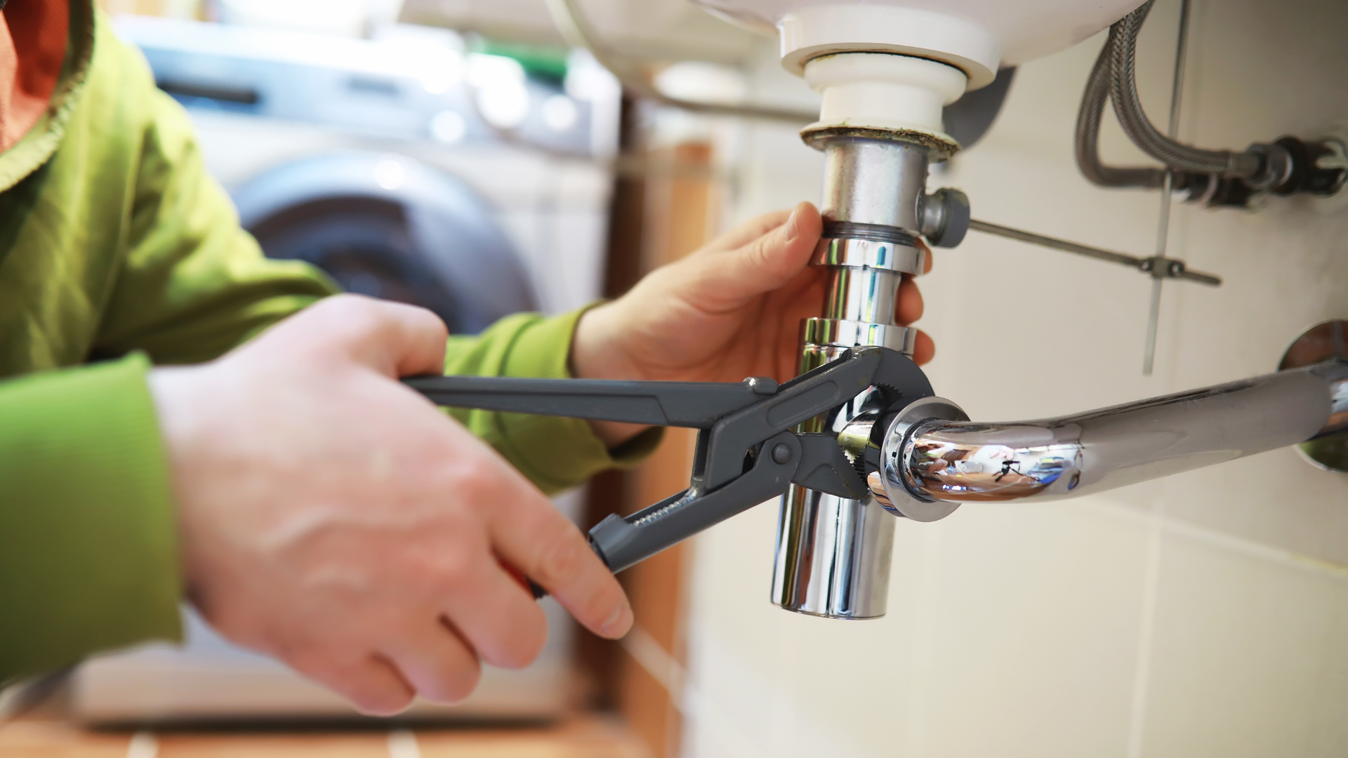 Person using adjustable pliers to tighten plumbing pipes under a sink.