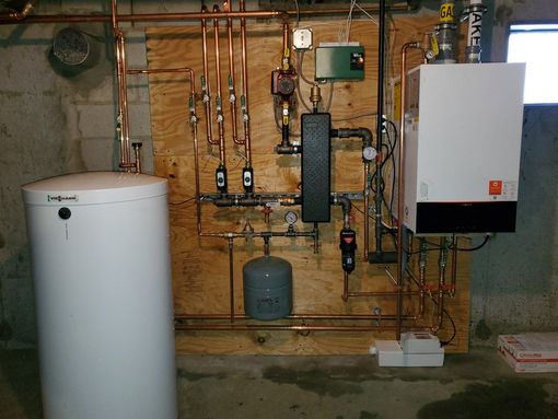 A home heating system with copper pipes, a water tank, and a white boiler on a wood panel.