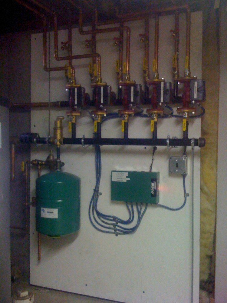 A boiler system on a white panel with copper pipes, green expansion tank, and control box.