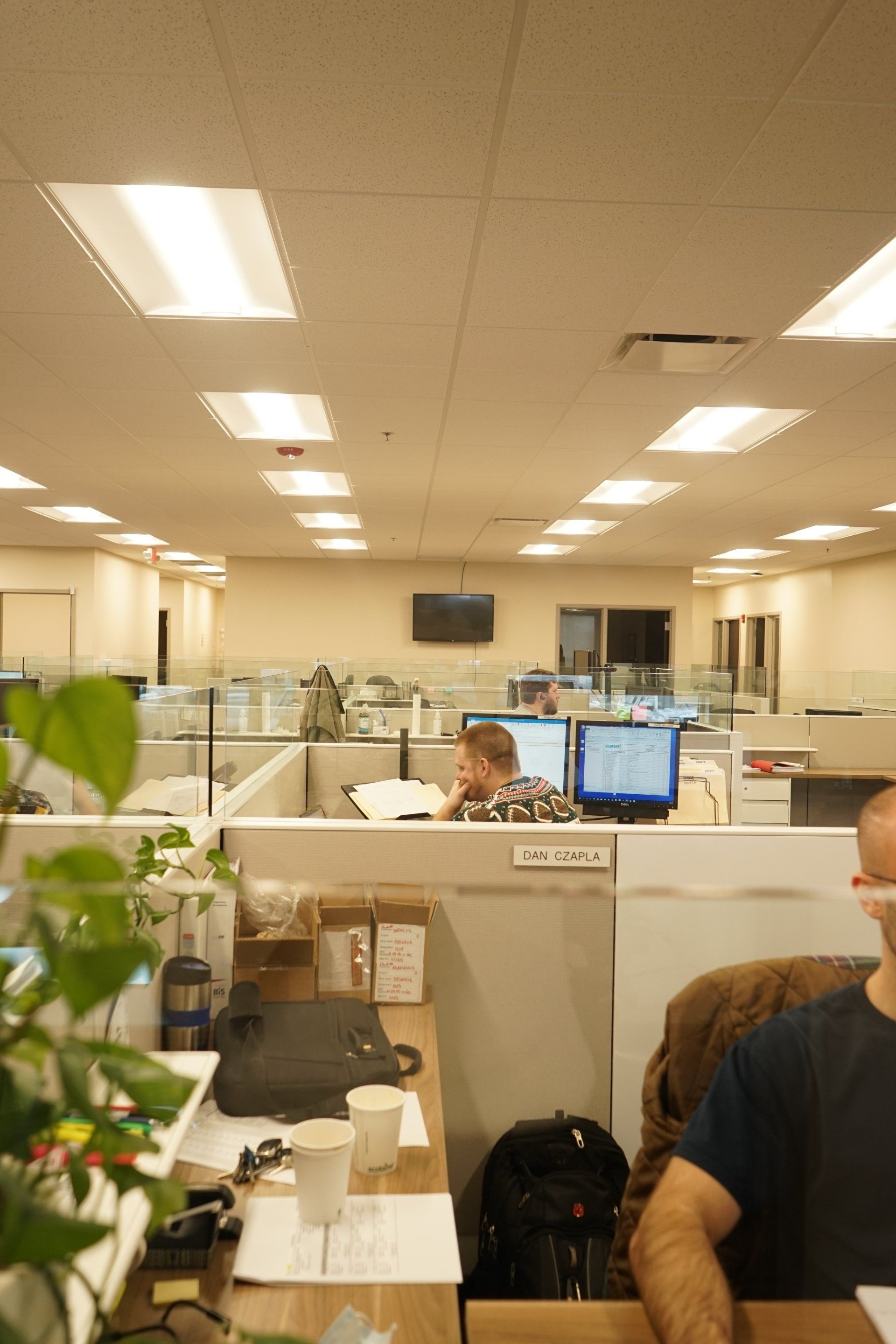 A man is sitting at a desk in a cubicle in an office.