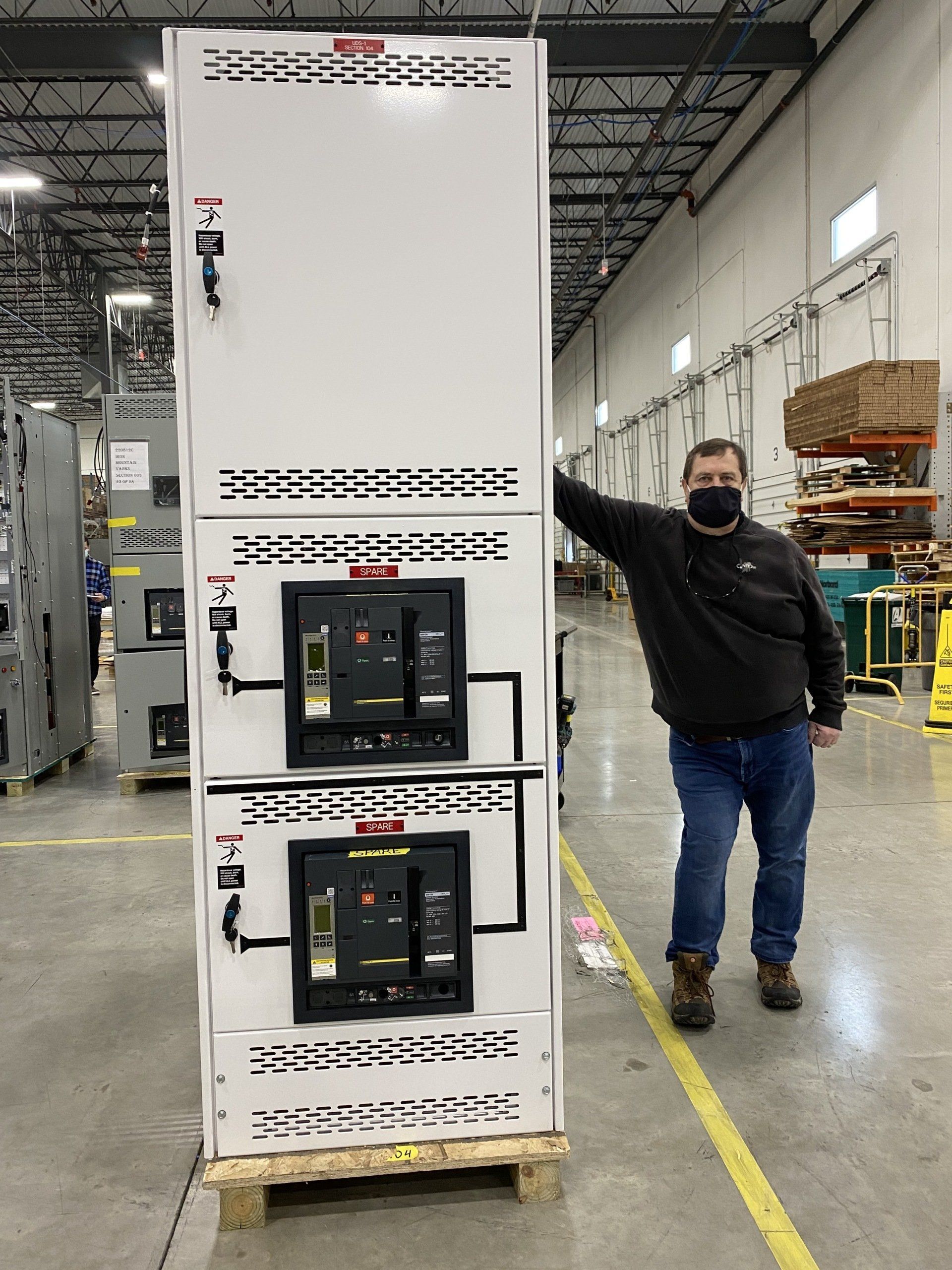 A man wearing a mask is standing in front of a large electrical box.