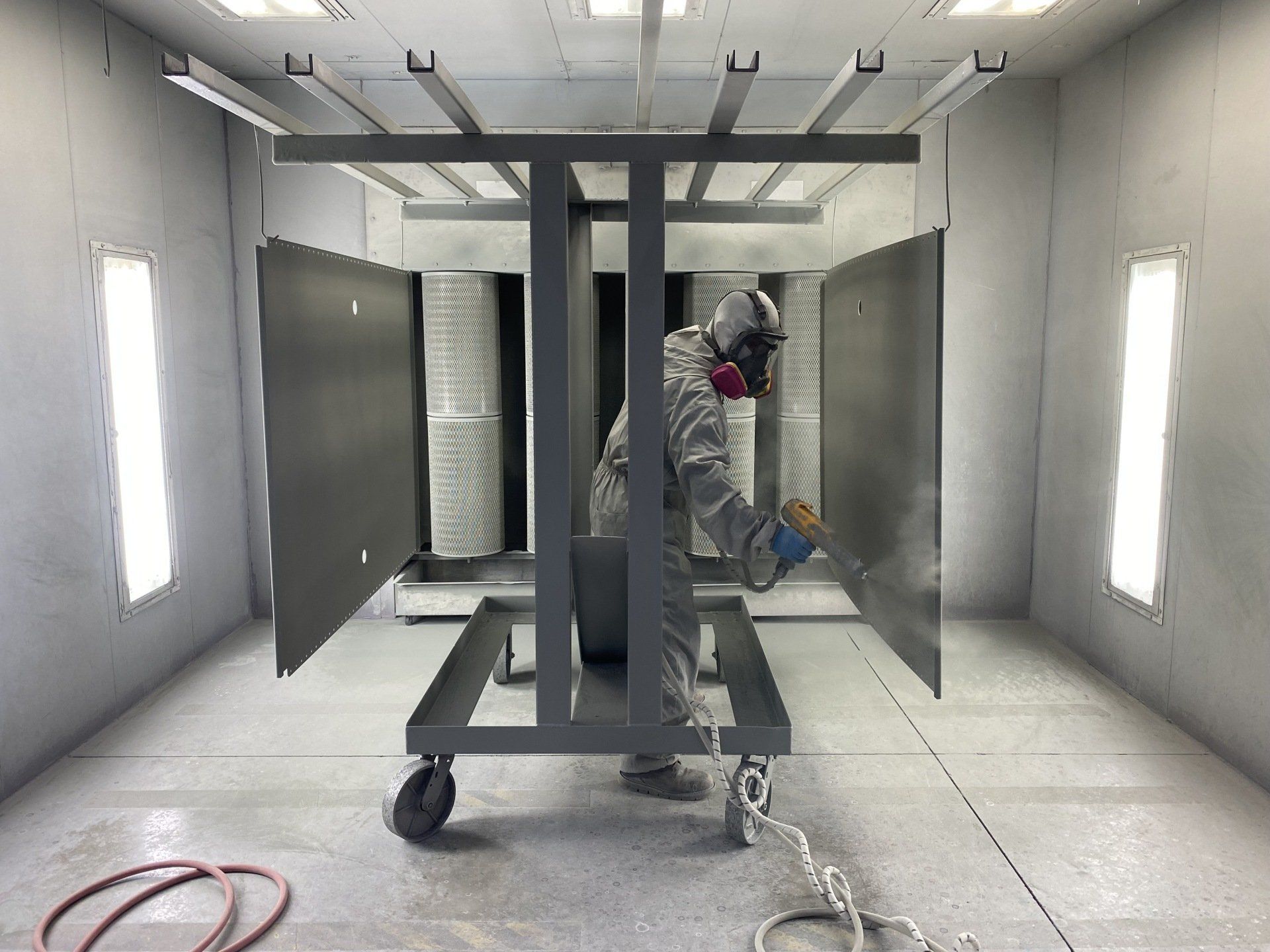 A man is painting a piece of metal in a paint booth.