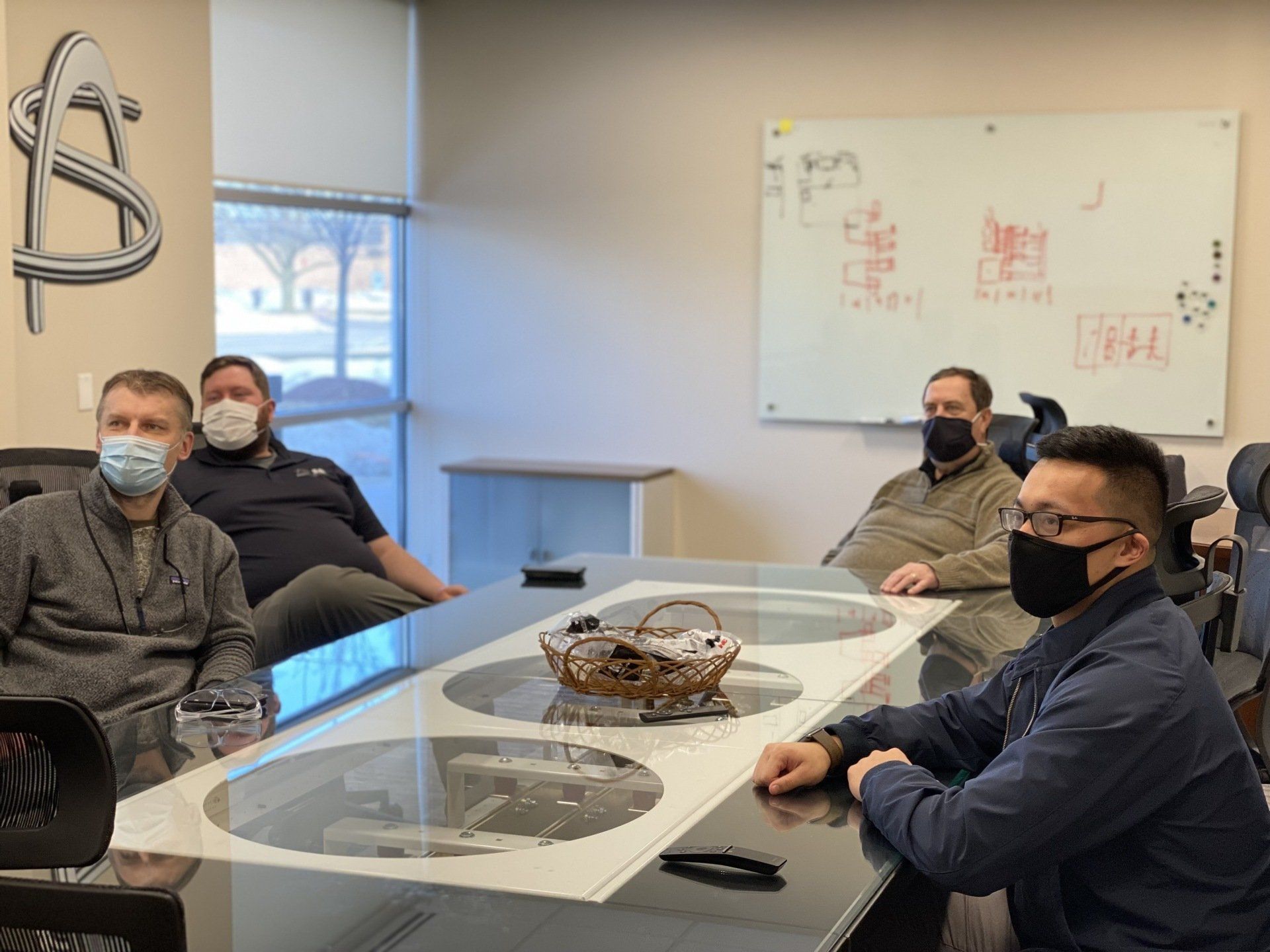 A group of men wearing face masks are sitting around a conference table.