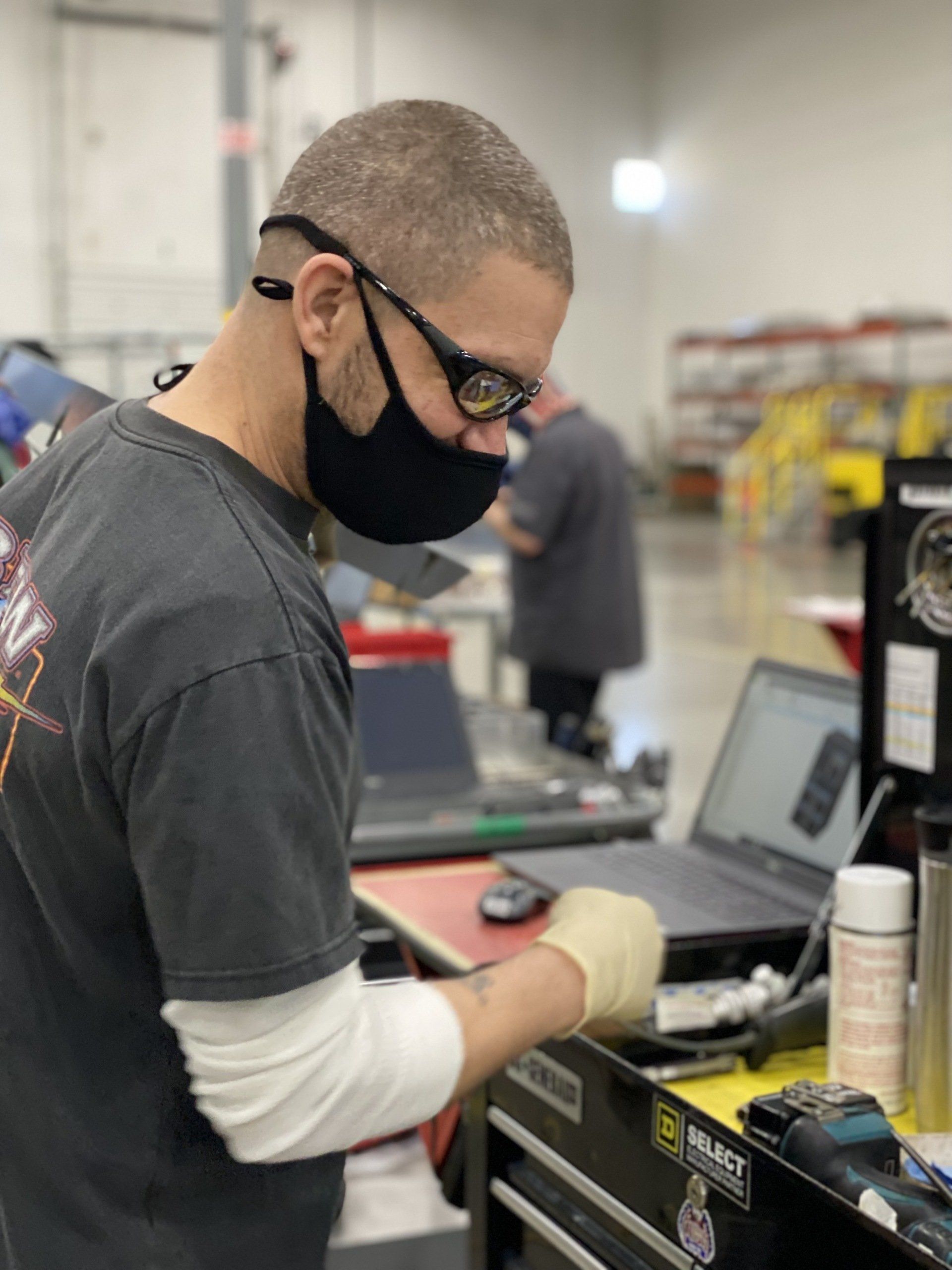 A man wearing a mask and glasses is working on a laptop.