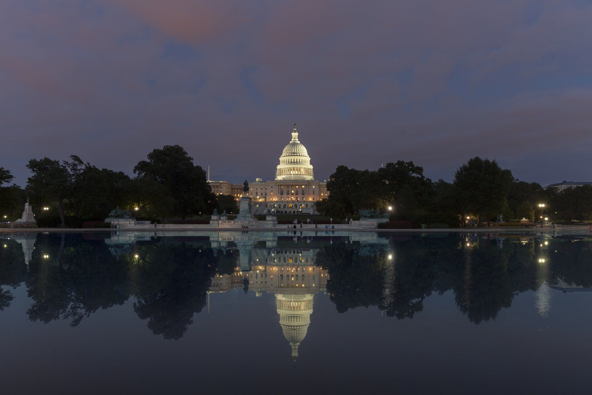 The capitol building is lit up at night and reflected in the water.