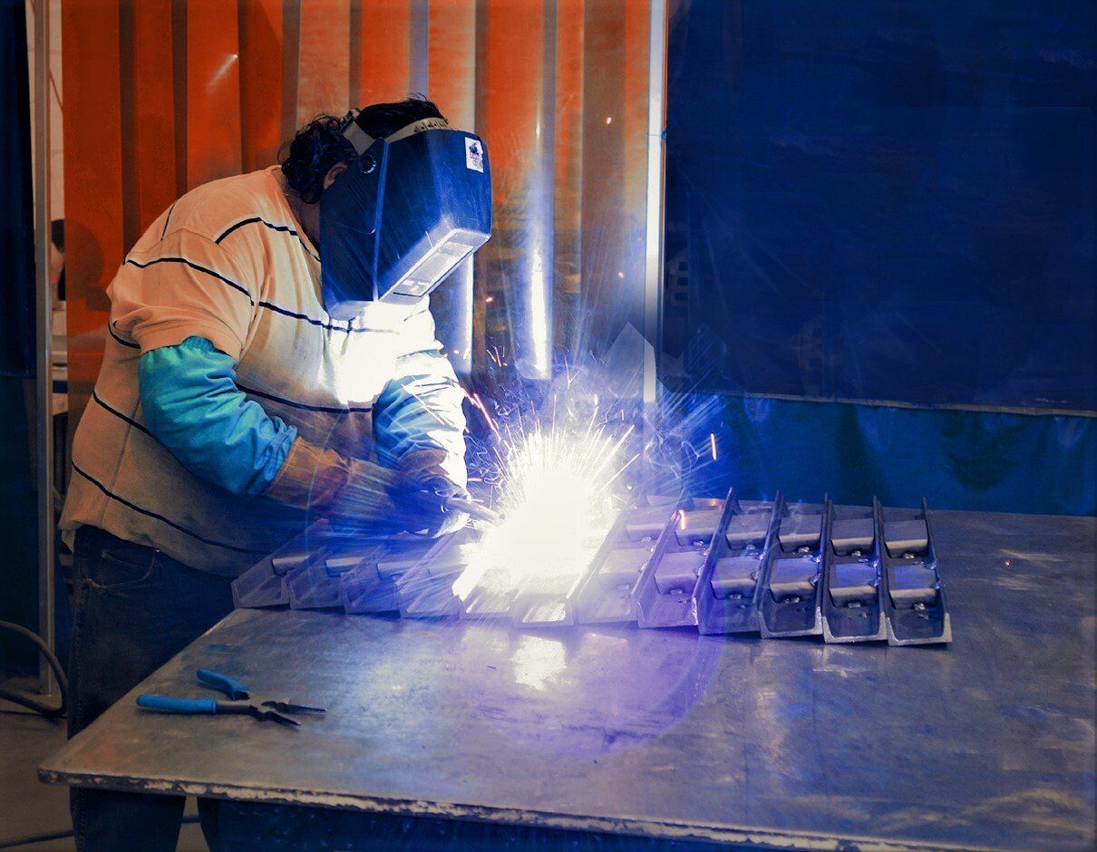 A man wearing a welding mask is welding a piece of metal.