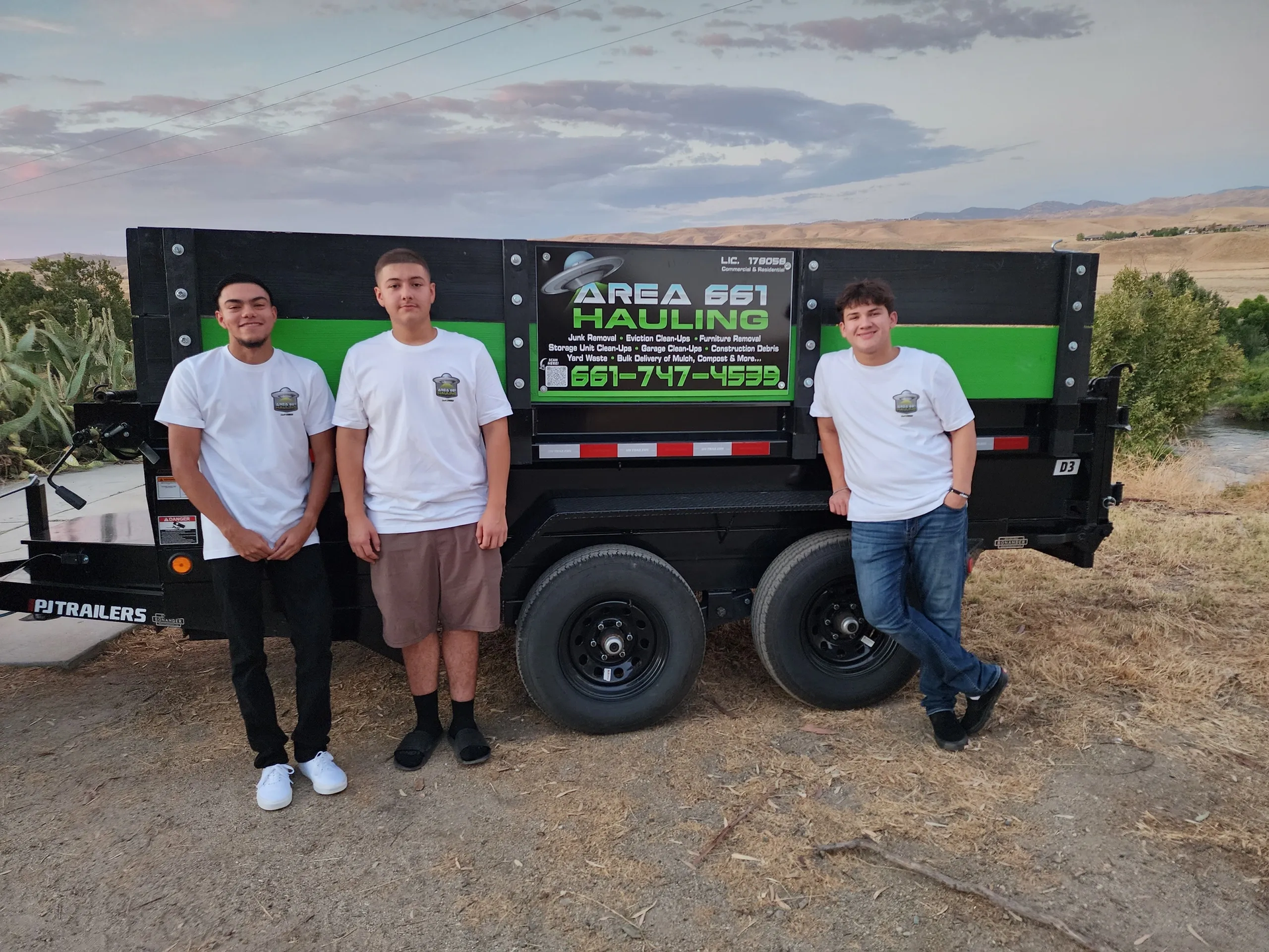 Three men are standing in front of a dumpster trailer.