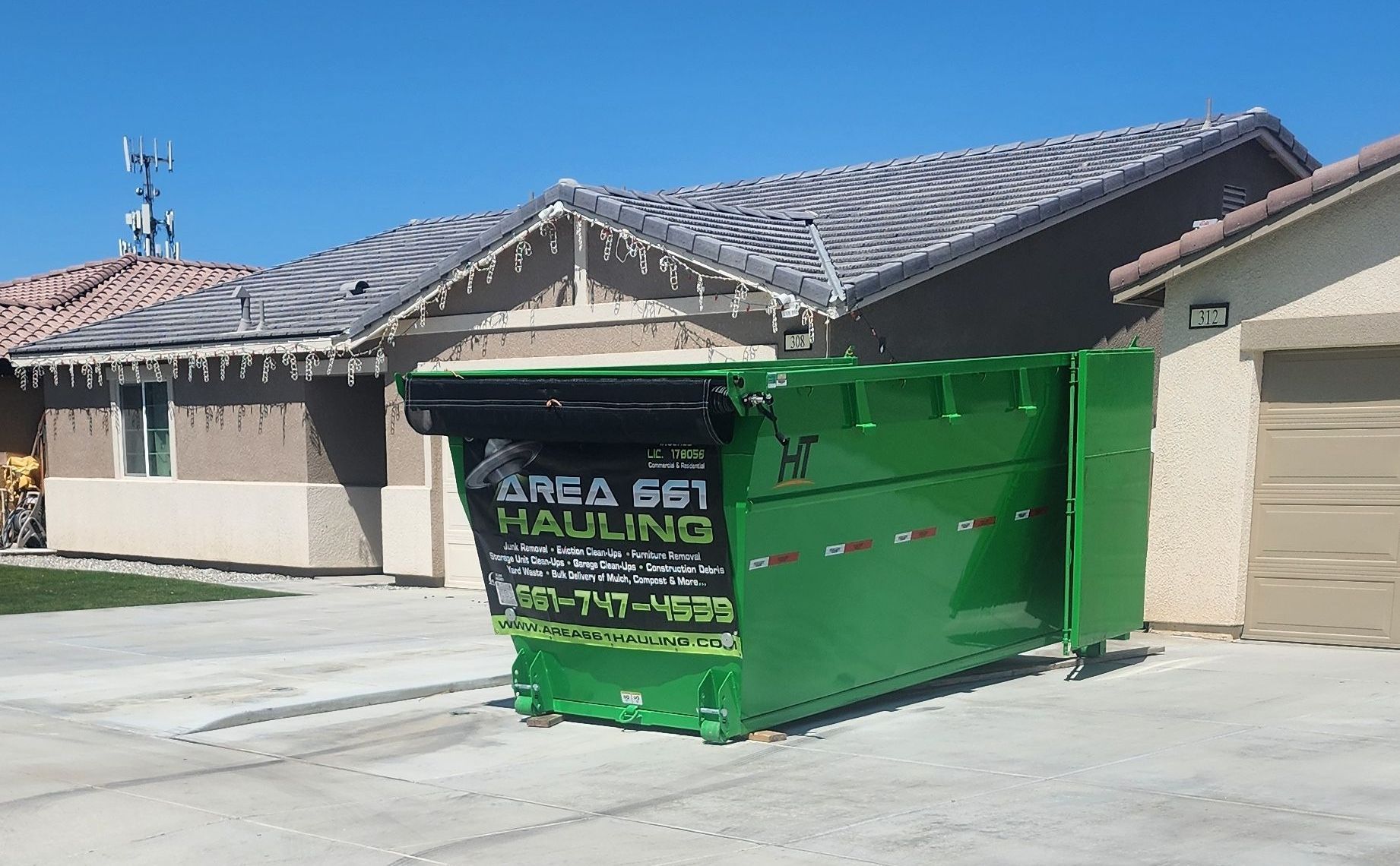 A beautiful green dumpster is parked in front of a Bakersfield house.