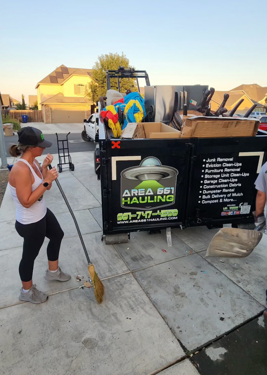 A woman is standing next to a dumpster that says area 661 Hauling