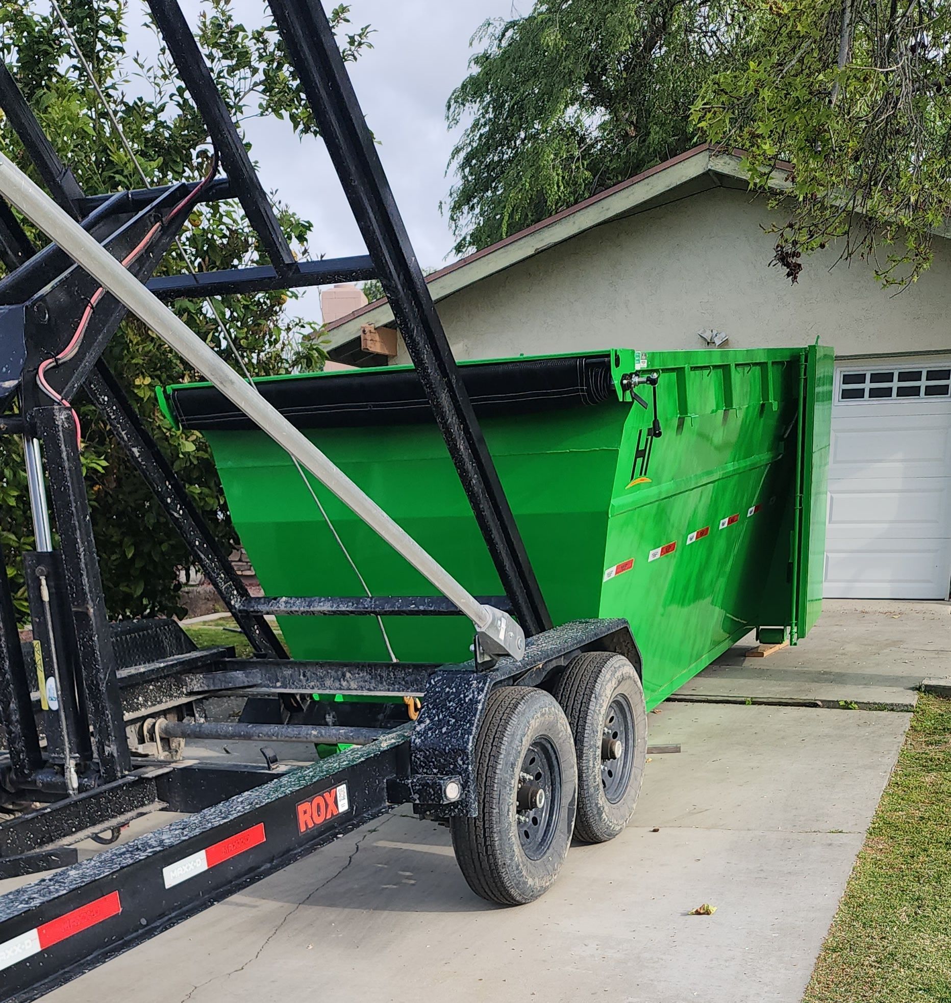 A green dumpster rental is on a trailer in front of a garage in Bakersfield, CA