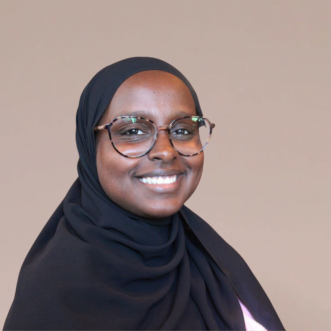 Kvinne med briller og svart hijab smilende, lyshudet med brune øyne. Beige bakgrunn.