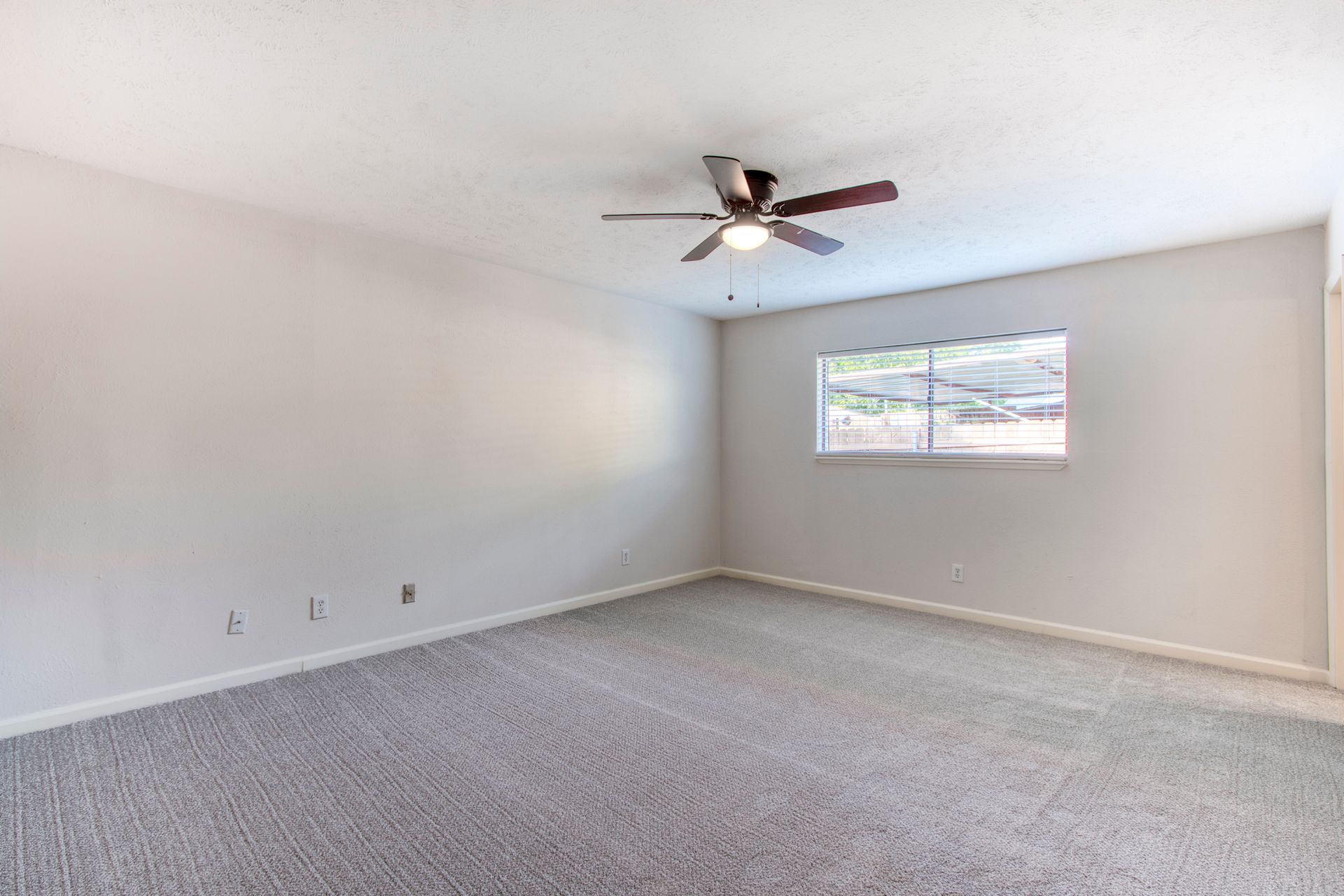 An empty room with a ceiling fan and a window.