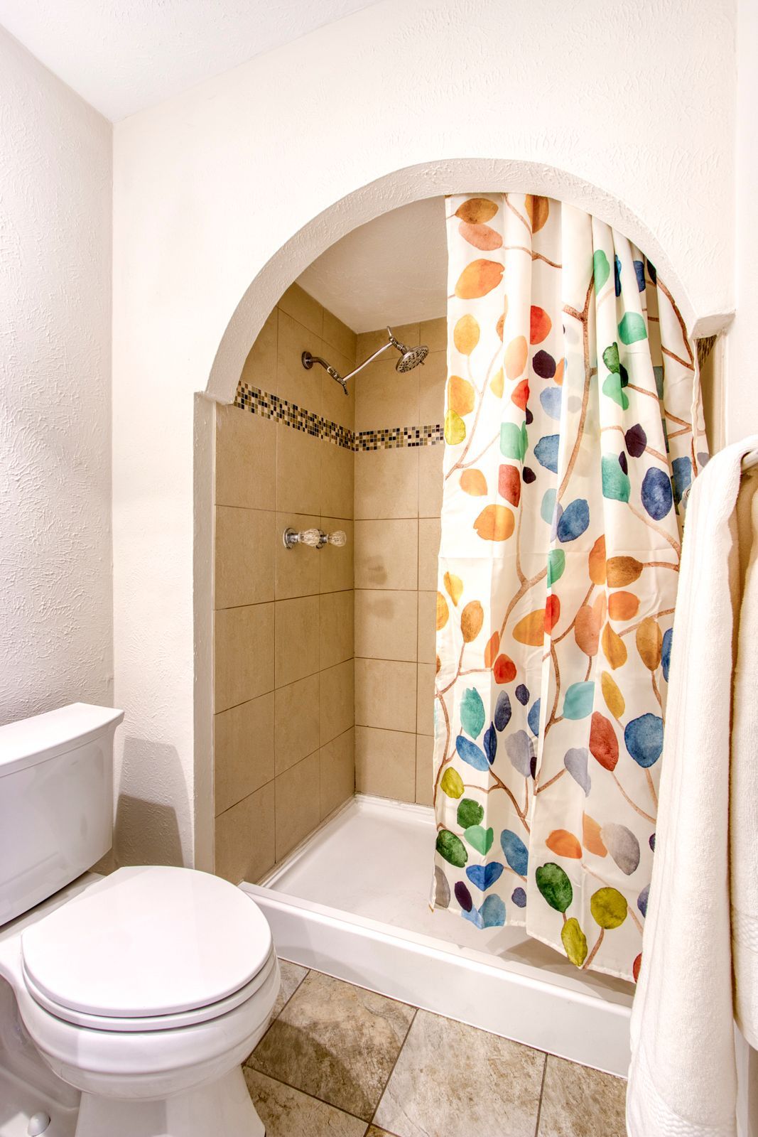 A bathroom with a toilet and shower with a colorful shower curtain