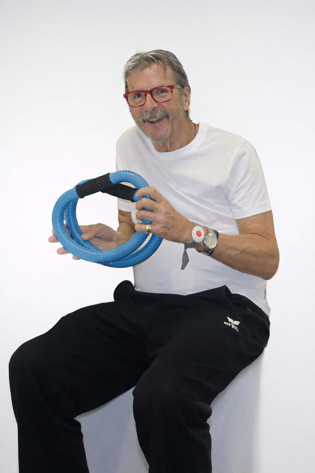 A person wearing glasses smiles while holding a coiled blue exercise tube with a black grip.