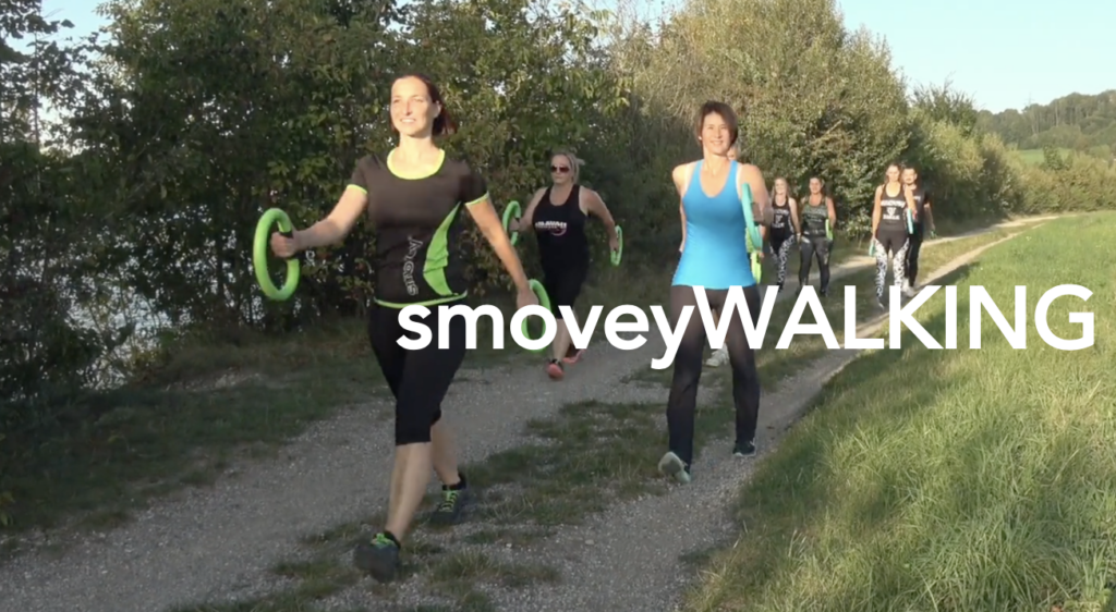 People walking on a dirt path in a sunny park, with “smoveyWALKING” text overlaid.