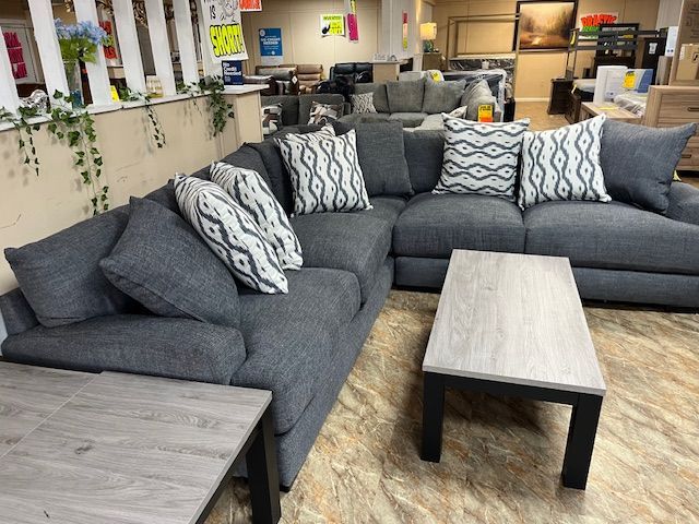 Gray sectional sofa with decorative pillows and wooden coffee tables in a furniture store.