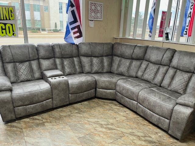Gray leather sectional sofa with diamond stitching and cup holders, in a showroom.