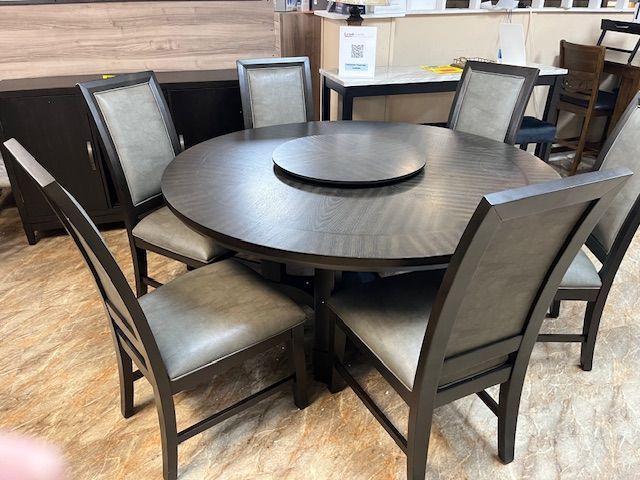 Round wooden dining table with eight chairs, gray upholstered seats, and a built-in lazy susan.
