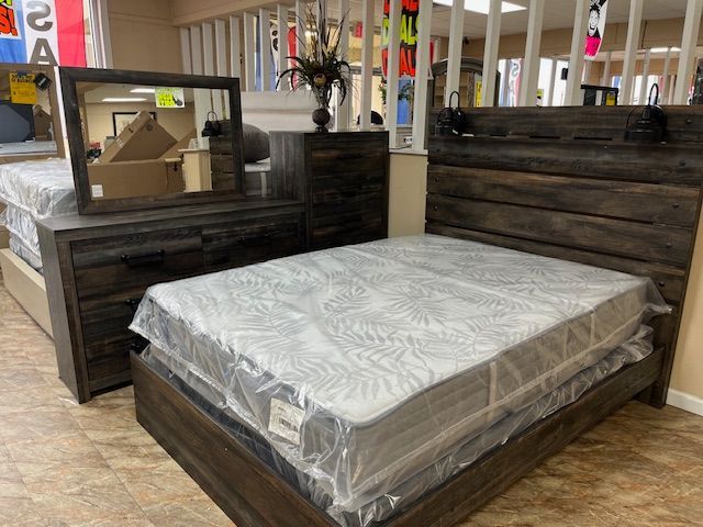 Bedroom furniture set, including a bed with mattress, dresser, and mirror, in a store setting.
