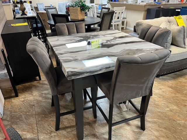 Square dining table with gray marble top, surrounded by four matching upholstered chairs.
