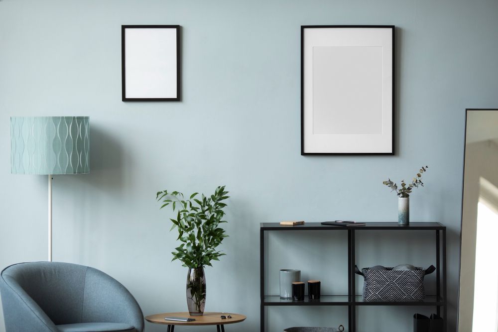 A living room with blue walls , a chair , a table , a lamp and a mirror.