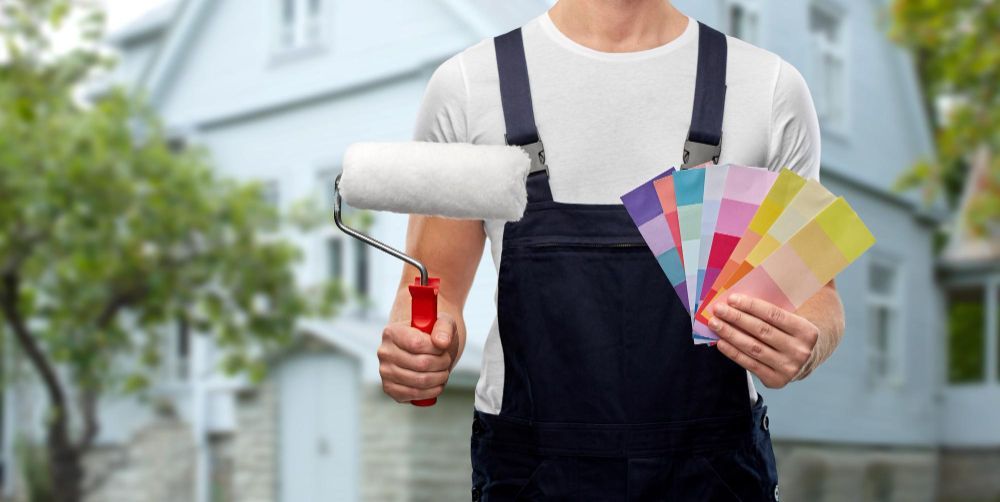 A man is holding a paint roller and a palette of paint.