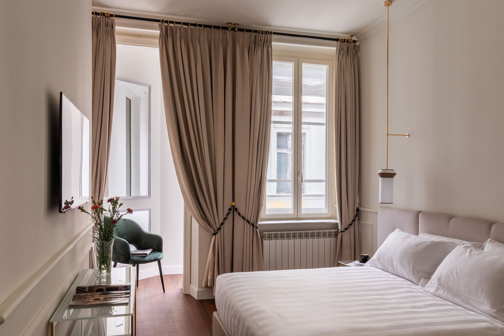 Bedroom with a bed, large windows with drapes, a TV on the wall, and a side chair.
