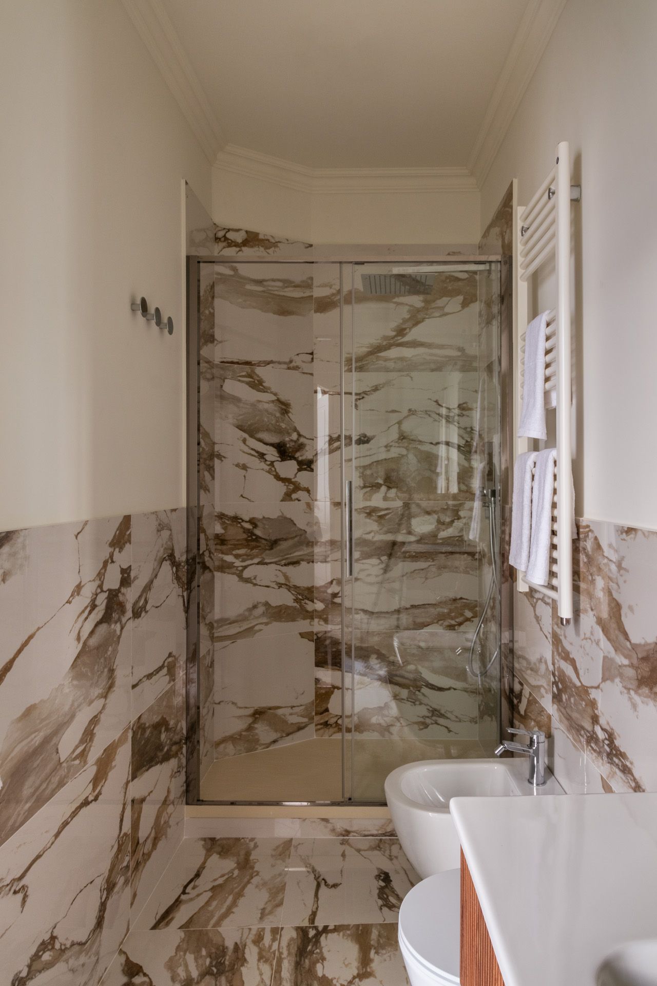 Bathroom with marble walls and floor, shower, towel rack, and bidet.