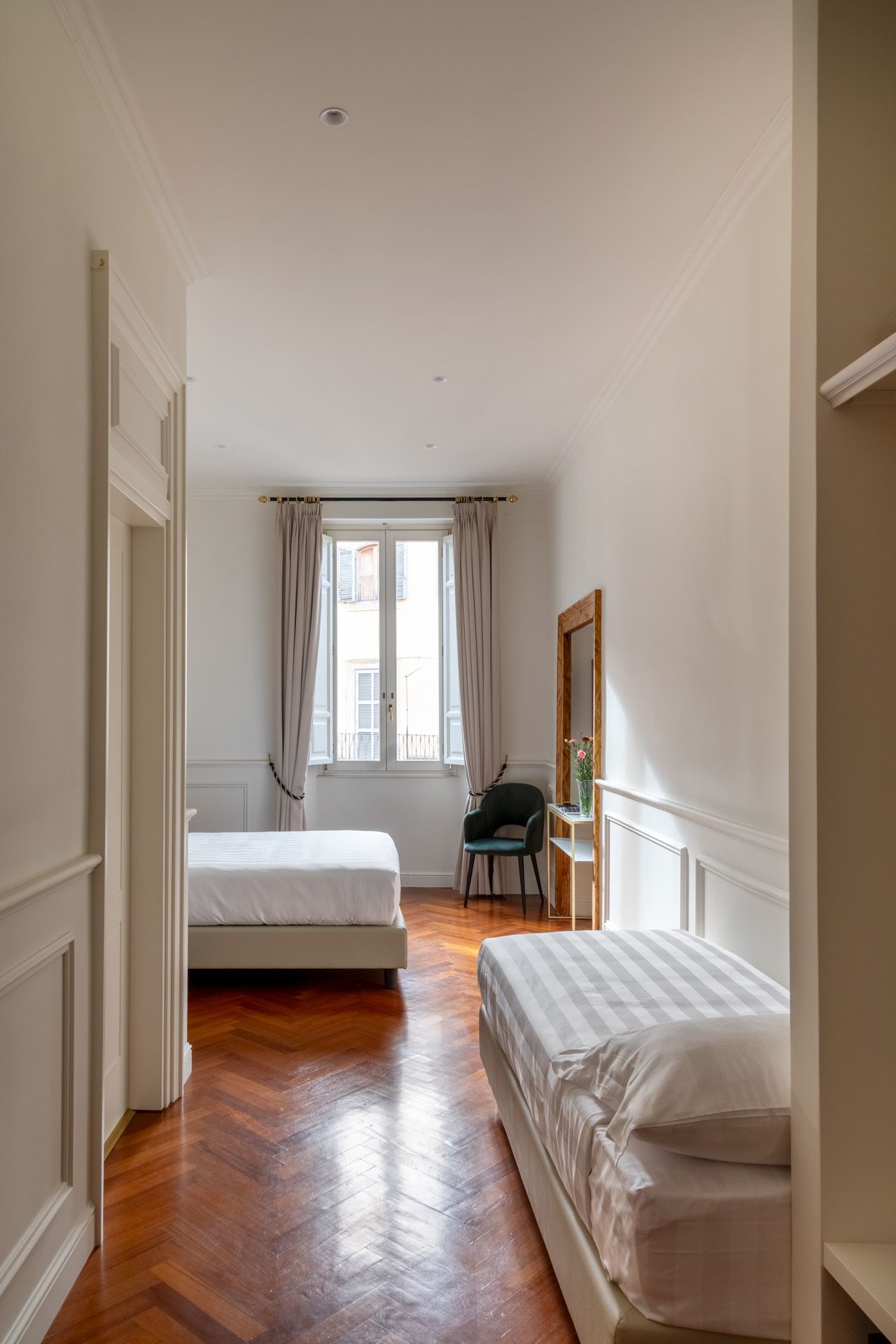 Narrow bedroom with two beds, window, and wood flooring. Bright, minimalist design.