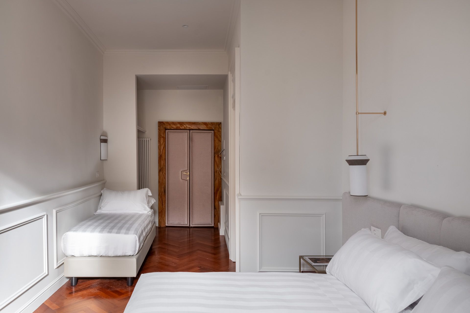 Bedroom with two beds, white walls, wood floor, and pink door.