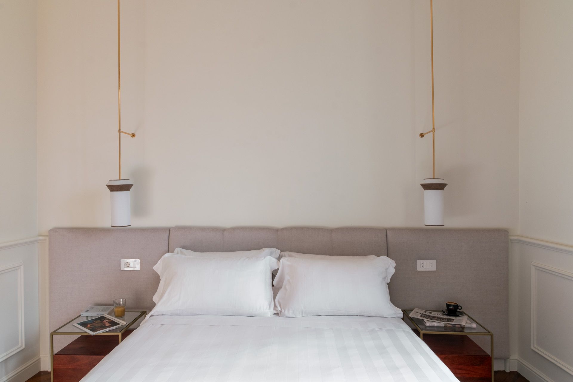 Bedroom with a bed, white linens, and bedside tables with lamps hanging overhead.